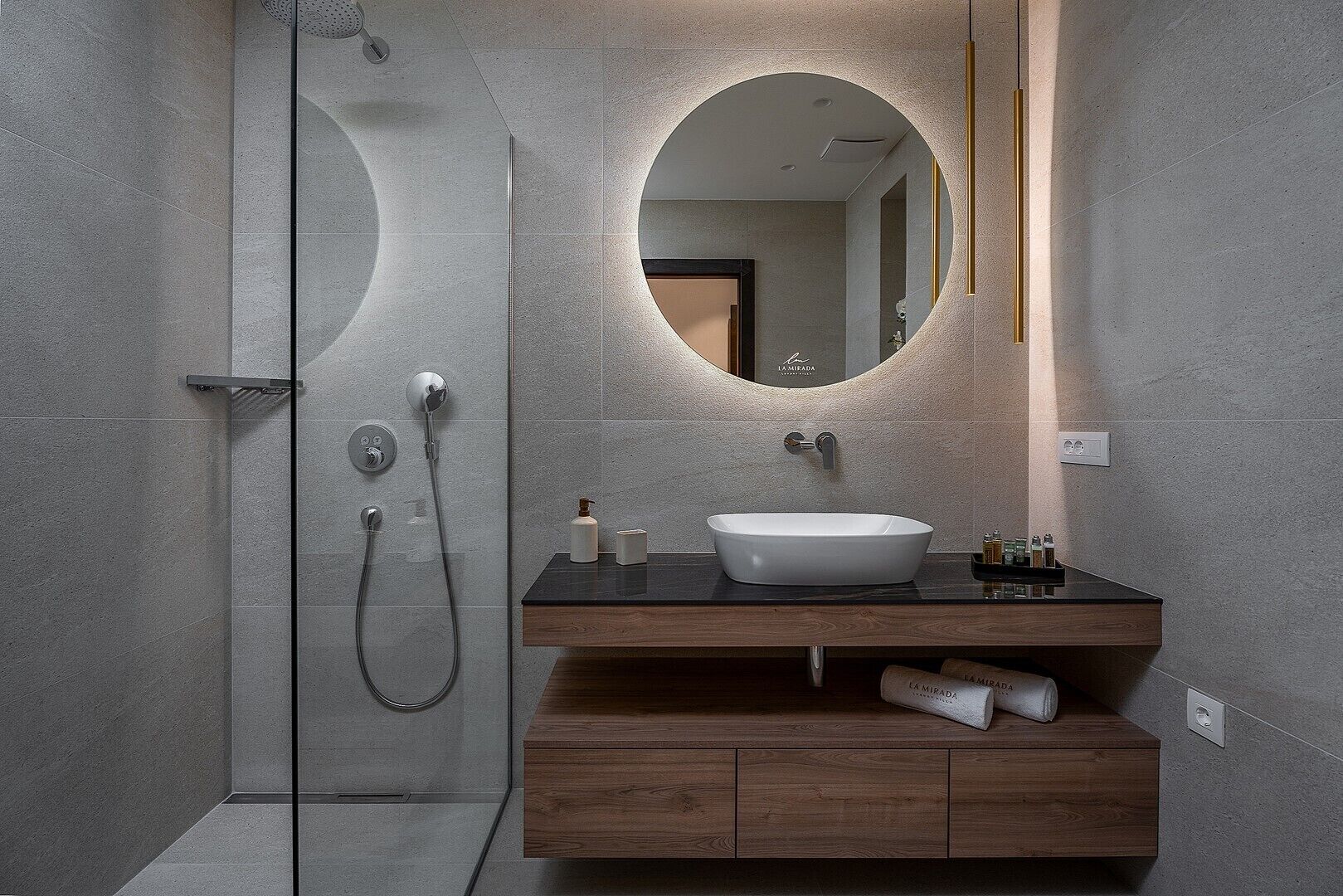 A modern bathroom with a freestanding shower, a round mirror, and a wooden vanity with a white sink.
