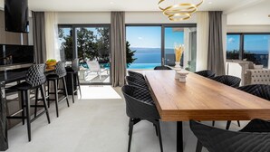 Un comedor moderno con una mesa de madera y sillas negras, ventanas amplias con vista al mar y un altavoz negro en la pared.