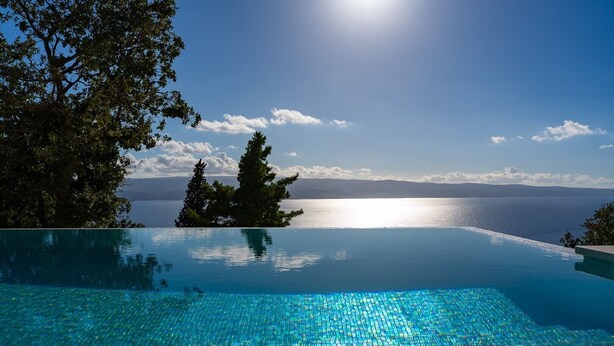 Una piscina infinita con una vista despejada del mar y montañas al fondo.