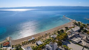 Vista aérea de una zona costera con playa, puerto deportivo y edificios.