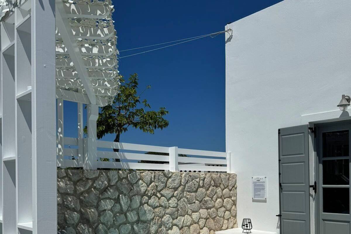 Ein moderner Poolbereich im Freien mit einer Steinwand, einer weißen Pergola und einer Tür zu einem Gebäude.
