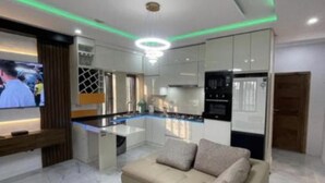 Uma sala de estar moderna com um sofá bege, uma TV de tela plana e uma área de cozinha com armários e bancada.