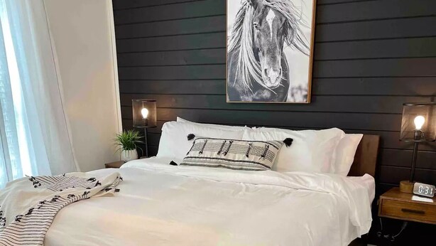 A bedroom with a large bed, a bench, a clock, and a wall-mounted lamp. - Stylish Richmond Home. Near EKU and Downtown (Richmond)