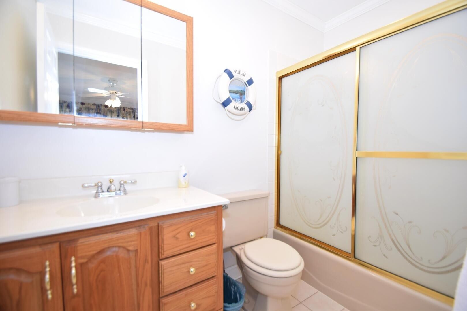 A bathroom with a wooden vanity, a white sink, a toilet, and a shower with a decorative glass door.