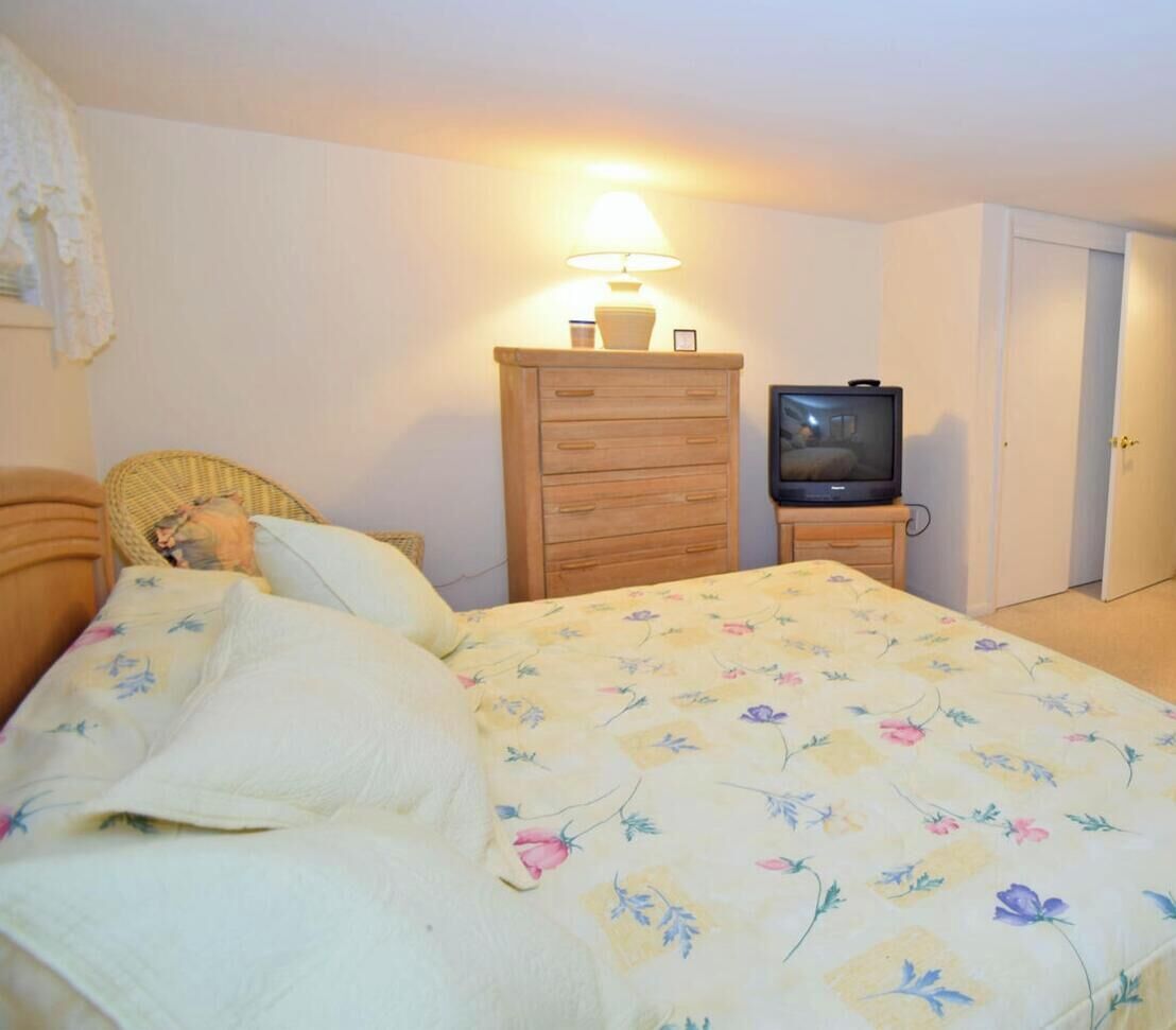 A bedroom with a bed, a wooden dresser, a television, and a lamp.