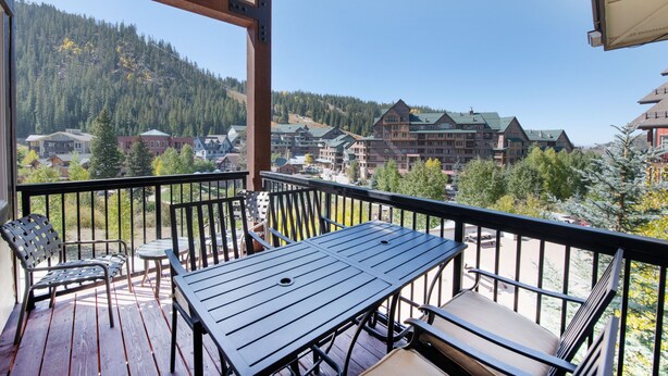 A wooden deck with a table and chairs, overlooking a mountainous area with buildings.