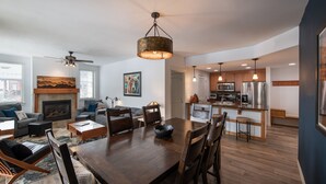 A spacious living room with a dark wooden dining table, comfortable seating, a fireplace, and a kitchen area with modern appliances.