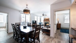 A spacious living room with a fireplace, a dining area with a wooden table and chairs, and a large window providing natural light.
