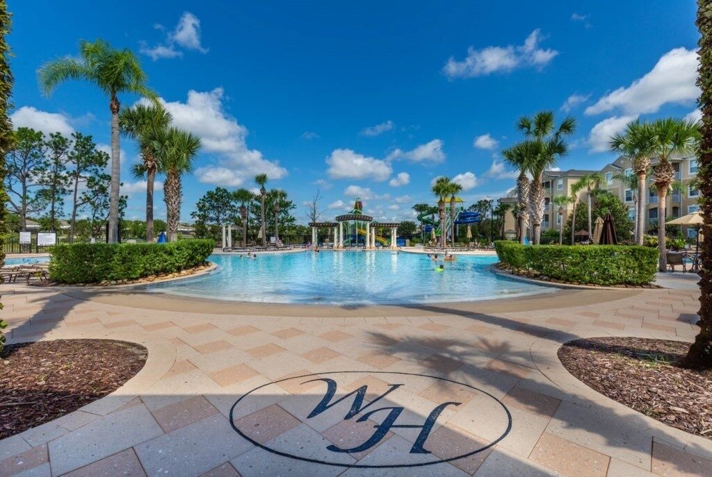 A pool area with palm trees, a gazebo, and a building with a 'WH' logo.