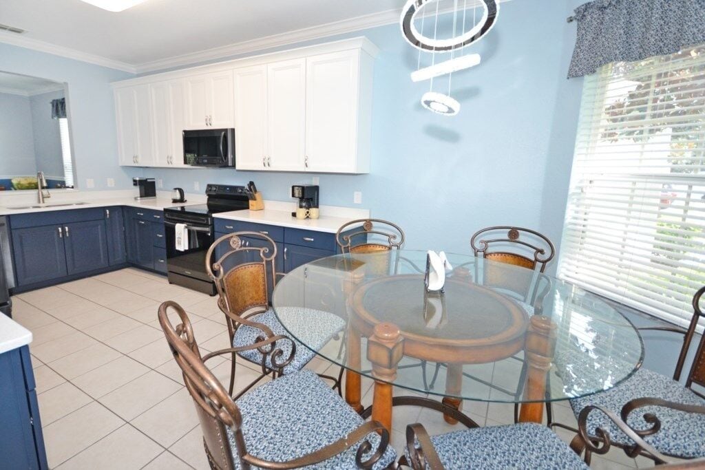 A modern kitchen with white cabinets, a black microwave, and a glass dining table with metal chairs.