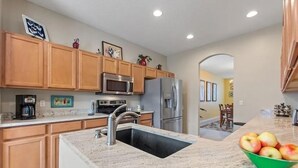 A kitchen with wooden cabinets, stainless steel appliances, a granite countertop, and a bowl of apples. - Henley Haven 6 Bedroom Villa by RedAwning (Davenport)
