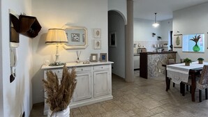 A modern kitchen with white cabinets, a dining area with a round table, and a living space with a white sofa and a decorative vase.
