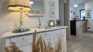 A modern kitchen with a white countertop, a decorative lamp, and a mirror above it. There are dried plants in front of the counter, and a stone island in the background.