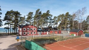 A red building with multiple windows, a tennis court, and a parking sign. - Varamons vandrarhem (Motala)