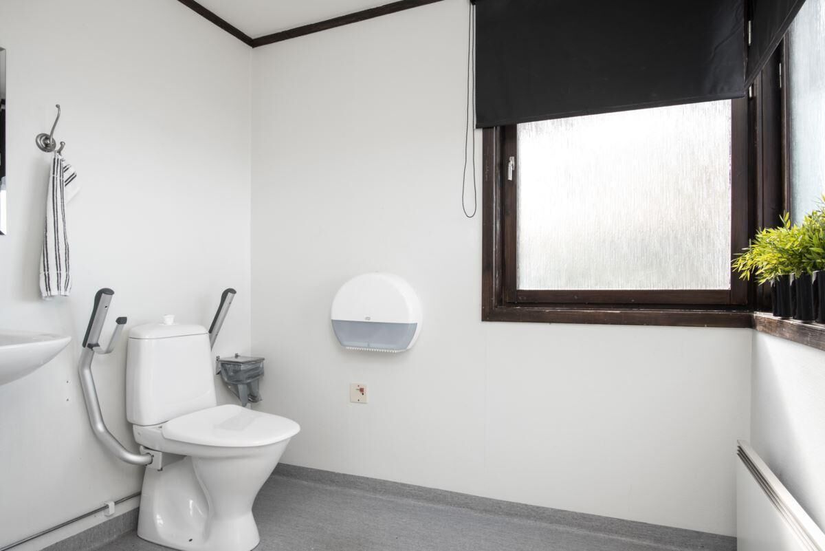 A bathroom with a toilet, a hand dryer, a sink, and a window with a black blind.