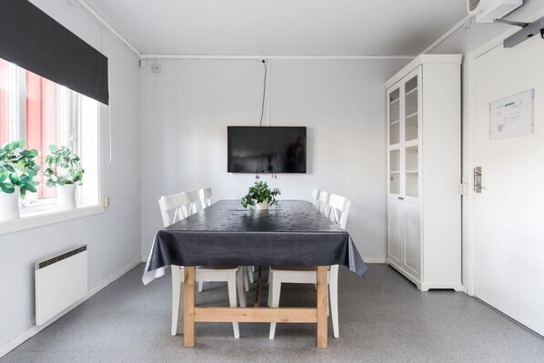 Un comedor con una mesa dispuesta para seis comensales, un televisor de pantalla plana montado en la pared, y un aparador blanco con puertas de cristal.