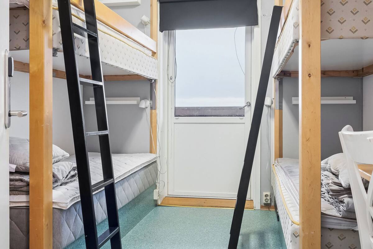 A dormitory room with bunk beds, a ladder, and a window.