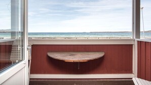 A balcony with a wooden bench, a glass door, and a view of the sea. - Varamons vandrarhem (Motala)