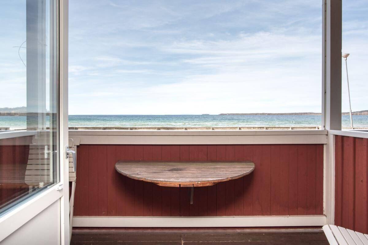 A balcony with a wooden bench, a glass door, and a view of the sea.