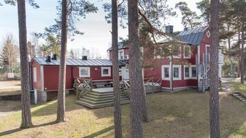 Ett rött hus i två våningar med ett tak av metall, omgivet av höga träd.