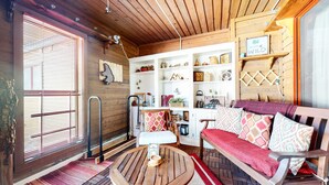 A cozy cabin interior with a wooden ceiling, a sofa with patterned cushions, a wooden coffee table, and a bookshelf filled with various decorative items.