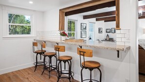 A kitchen with a white interior, wooden bar stools, and a large window.