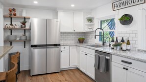 A kitchen with white cabinets, stainless steel appliances, and a farmhouse sign.