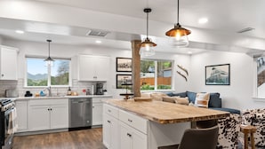 A modern kitchen with white cabinets, a wooden island, and pendant lighting.