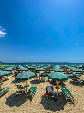 Una playa con hileras de sombrillas verdes y sillas reclinables.