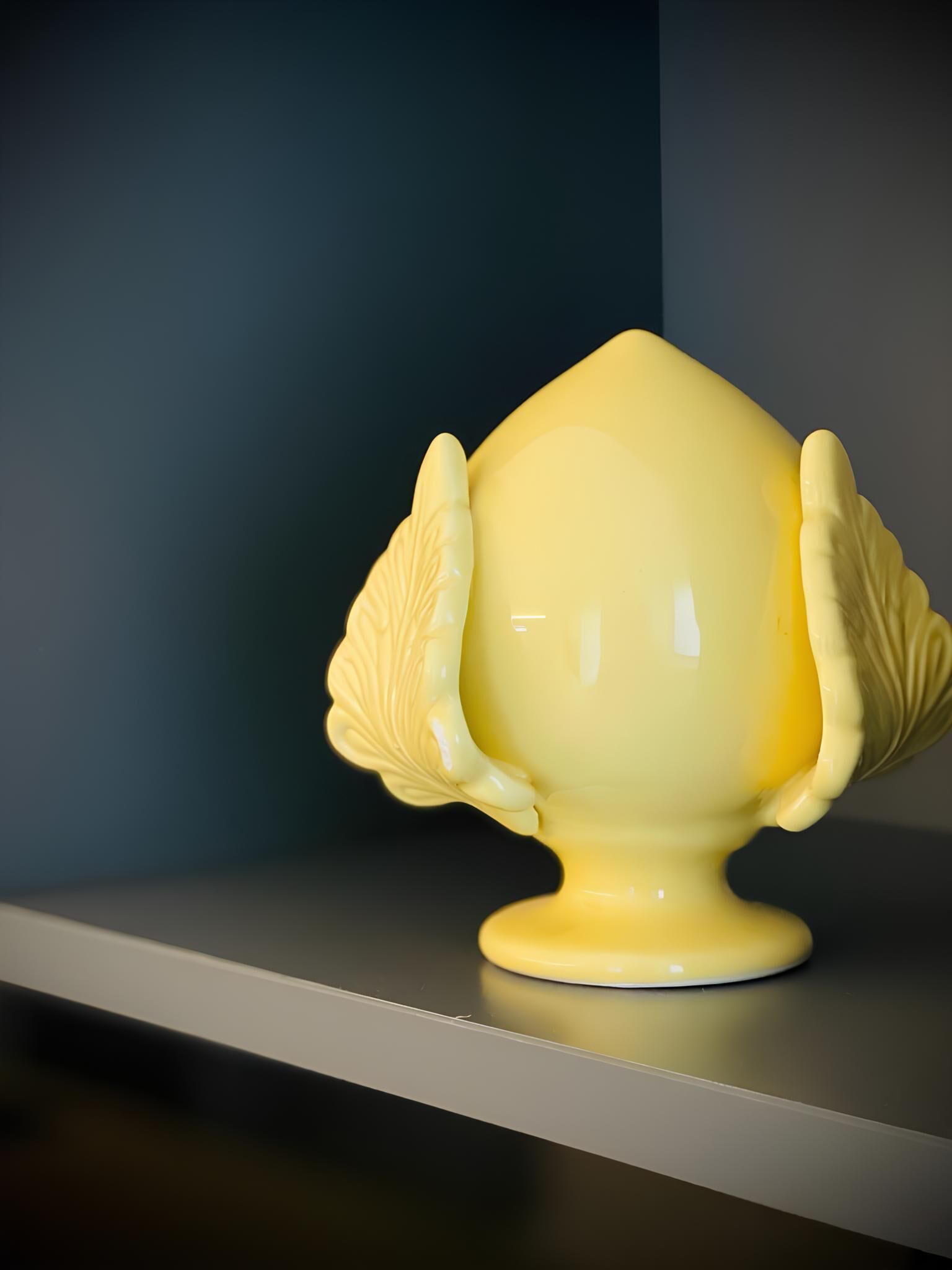 A yellow ceramic object with leaf-like designs on its sides, placed on a shelf.