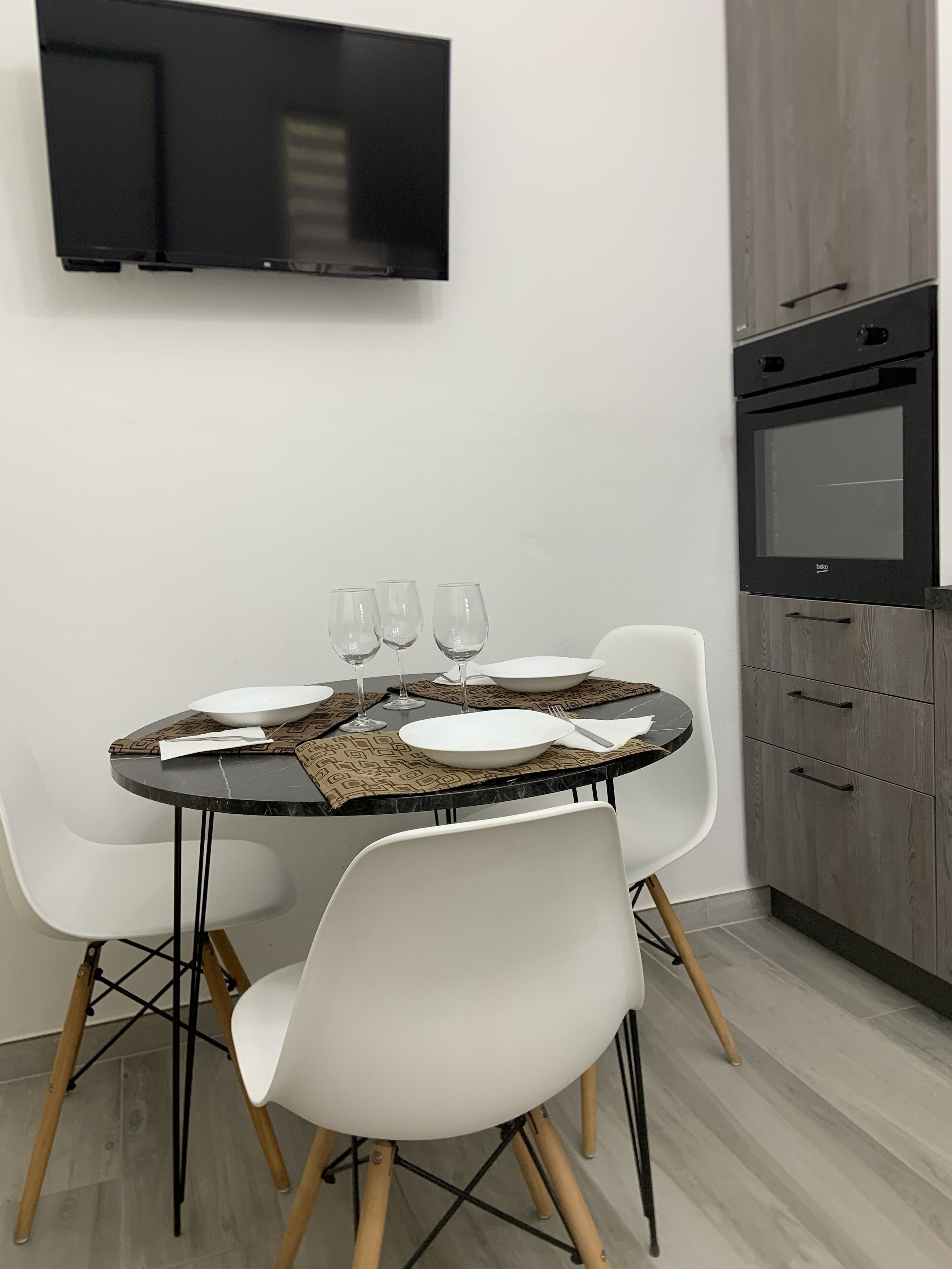 A modern dining area with a round table, white chairs, and a flat-screen TV mounted on the wall.