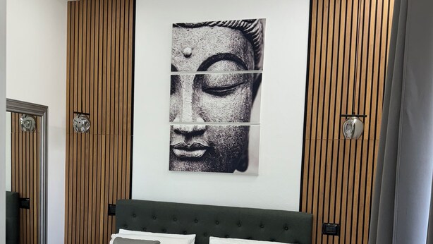 Et moderne soveværelse med en stor seng, træpaneler på væggene og en Buddha-statue.