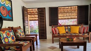 A living room with two wooden sofas, colorful cushions, a coffee table, and a large fish painting on the wall. - Casa Jacarandá - Casa completa (Ipojuca)