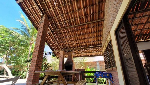 An outdoor patio with a brick wall, a wooden table, and a grill. - Casa Jacarandá - Casa completa (Ipojuca)