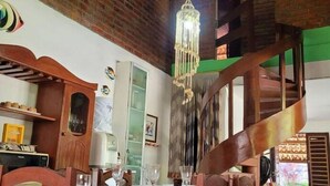 A dining area with a brick wall, a chandelier, wooden chairs, and a table set for a meal. - Casa Jacarandá - Casa completa (Ipojuca)