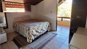 A bedroom with a wooden ceiling, a bed with a patterned bedspread, a small bedside table, and a window with blinds. - Casa Jacarandá - Casa completa (Ipojuca)