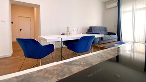 Una sala moderna con un sofá blanco, una mesa de centro de vidrio y sillas azules.