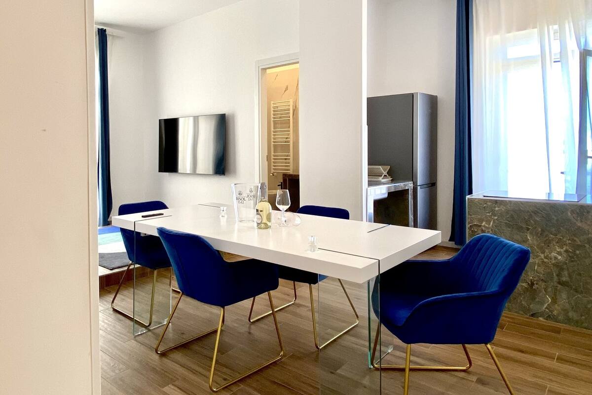A modern dining area with a white table, blue chairs, and a flat-screen TV mounted on the wall.