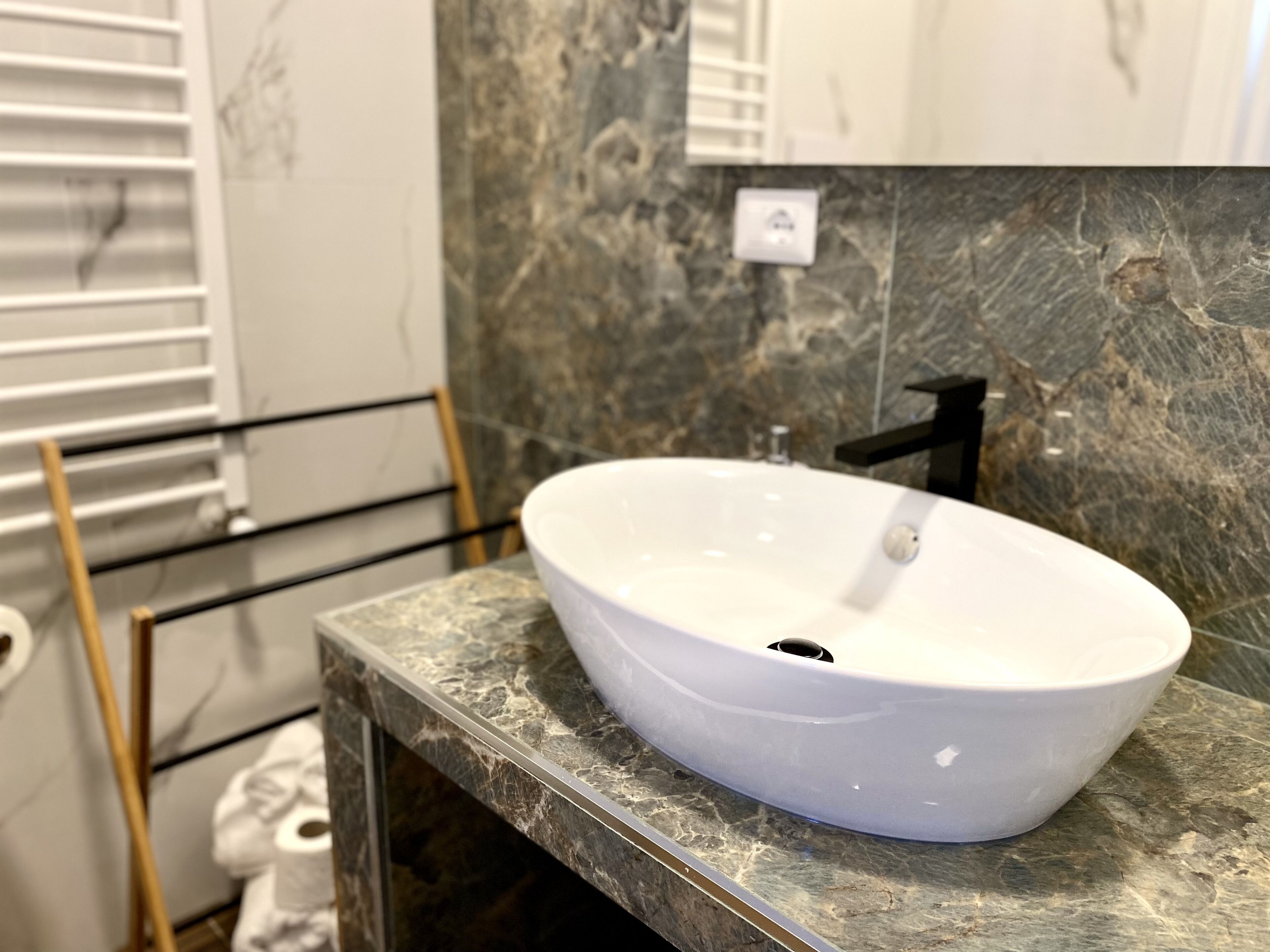 Une salle de bain avec un lavabo sur colonne blanc, posé sur un plan de travail en marbre, un robinet noir et un porte-serviettes avec une serviette blanche.