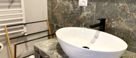 A bathroom with a white vessel sink on a marble countertop, a black faucet, and a towel rack with a white towel.