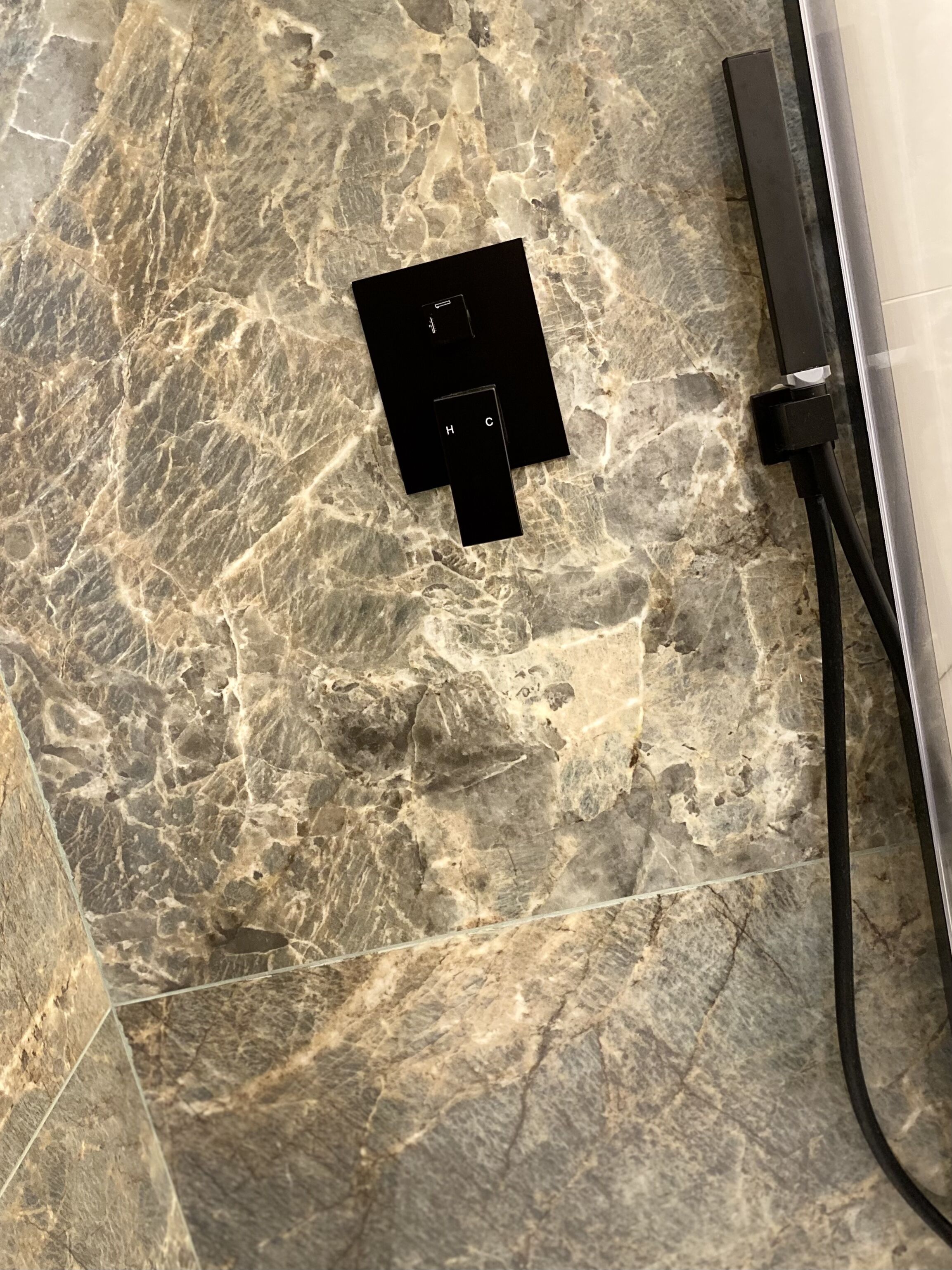 Een badkamer met een marmeren vloer, een zwart stopcontact en een douche slang.