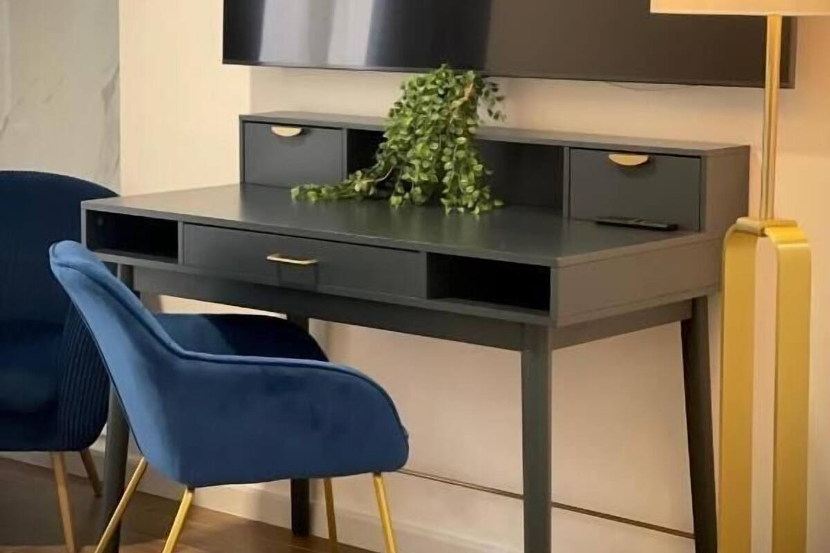 A modern room with a dark desk, two blue chairs, a TV mounted on the wall, and a floor lamp.