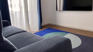 Una sala de estar moderna con un sofá gris, un tapete azul y verde, y un televisor de pantalla plana grande montado en la pared.