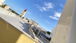 Vista desde una ventana de un edificio, con cielo despejado, una torre del reloj y un cuerpo de agua al fondo.