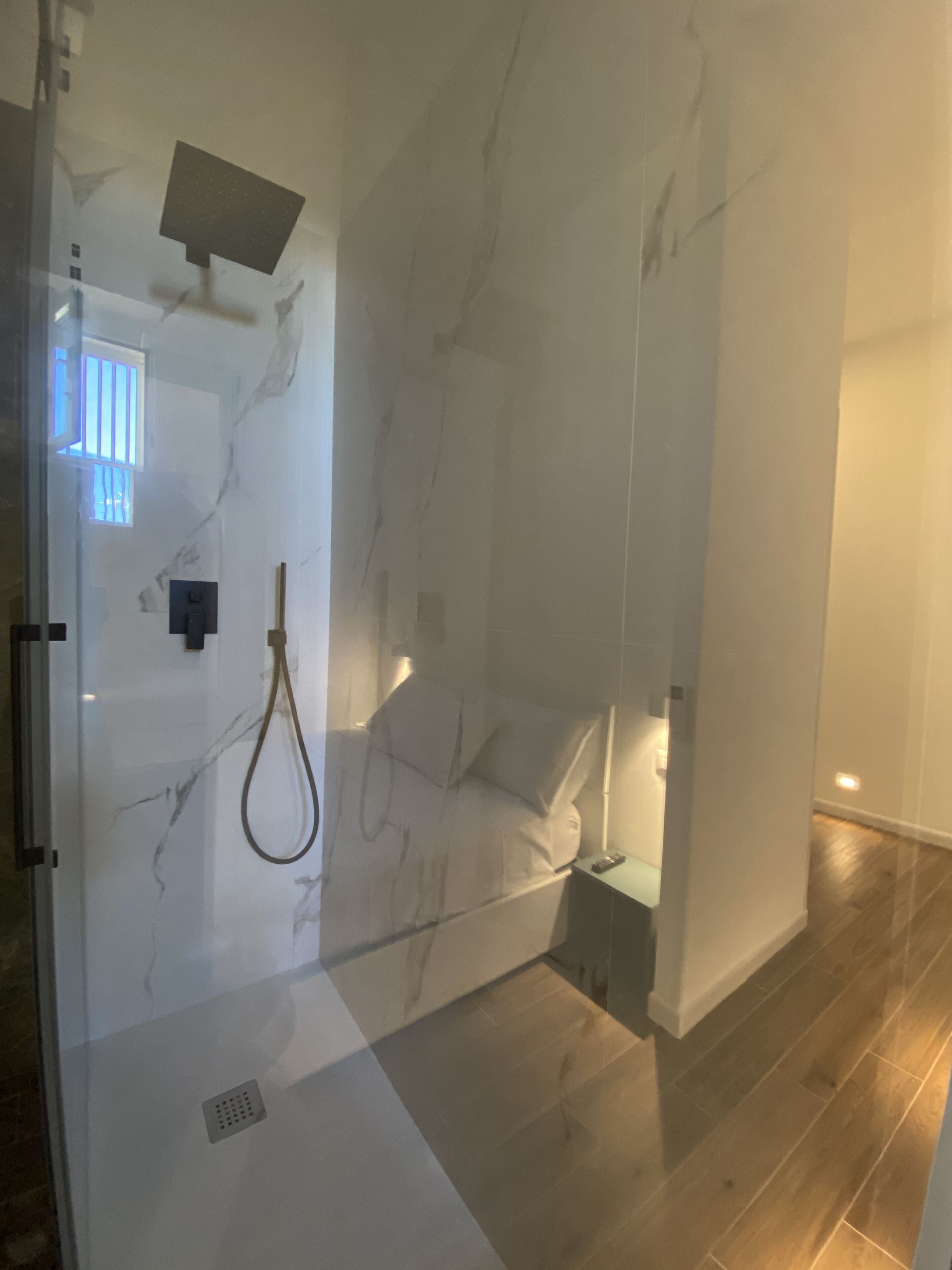 A modern bathroom with a glass-enclosed shower, marble walls, and a wooden floor.