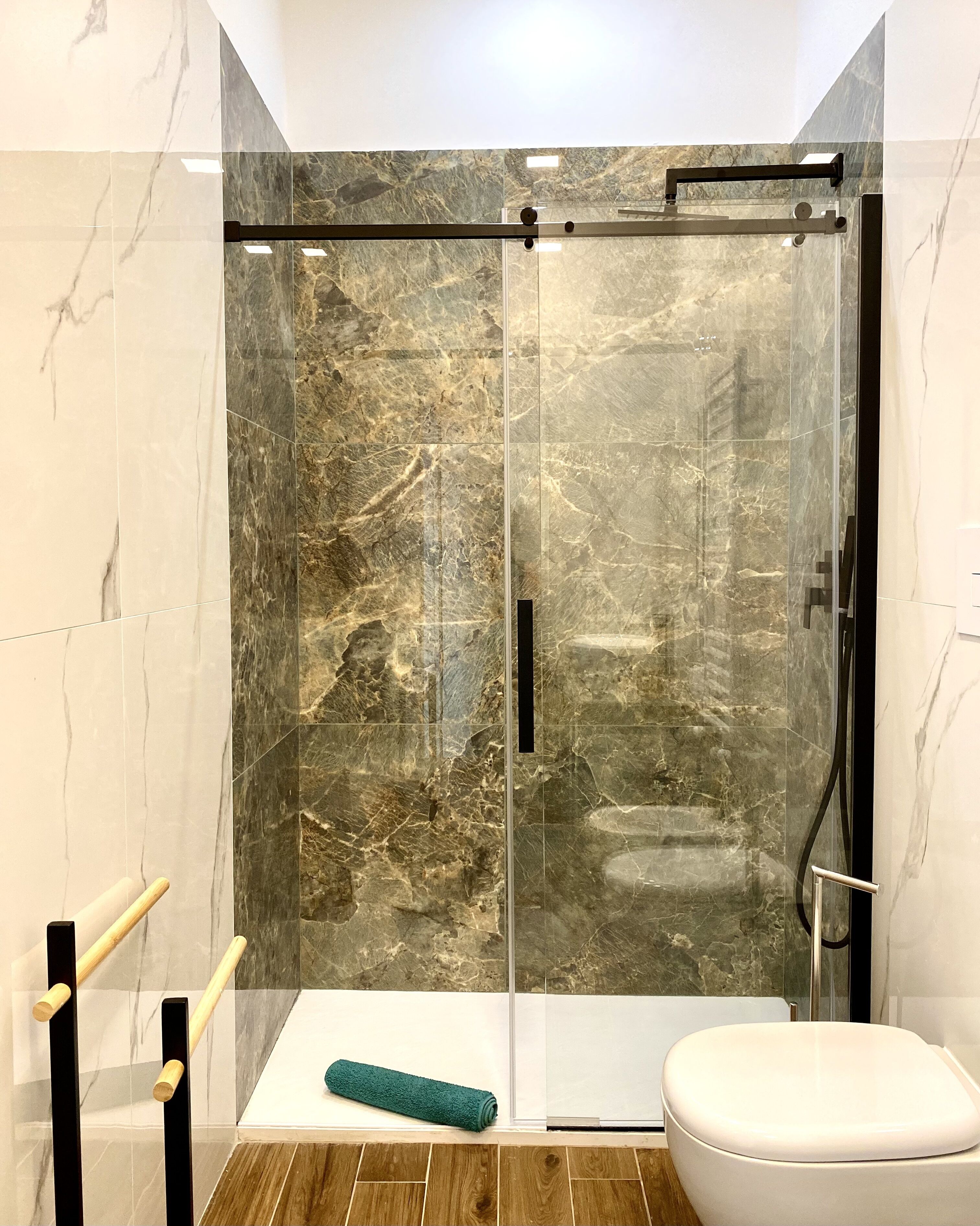 A modern bathroom with a glass shower enclosure, a white toilet, and a wooden floor.