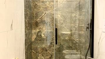 A modern bathroom with a glass shower enclosure, a white toilet, and a wooden floor.