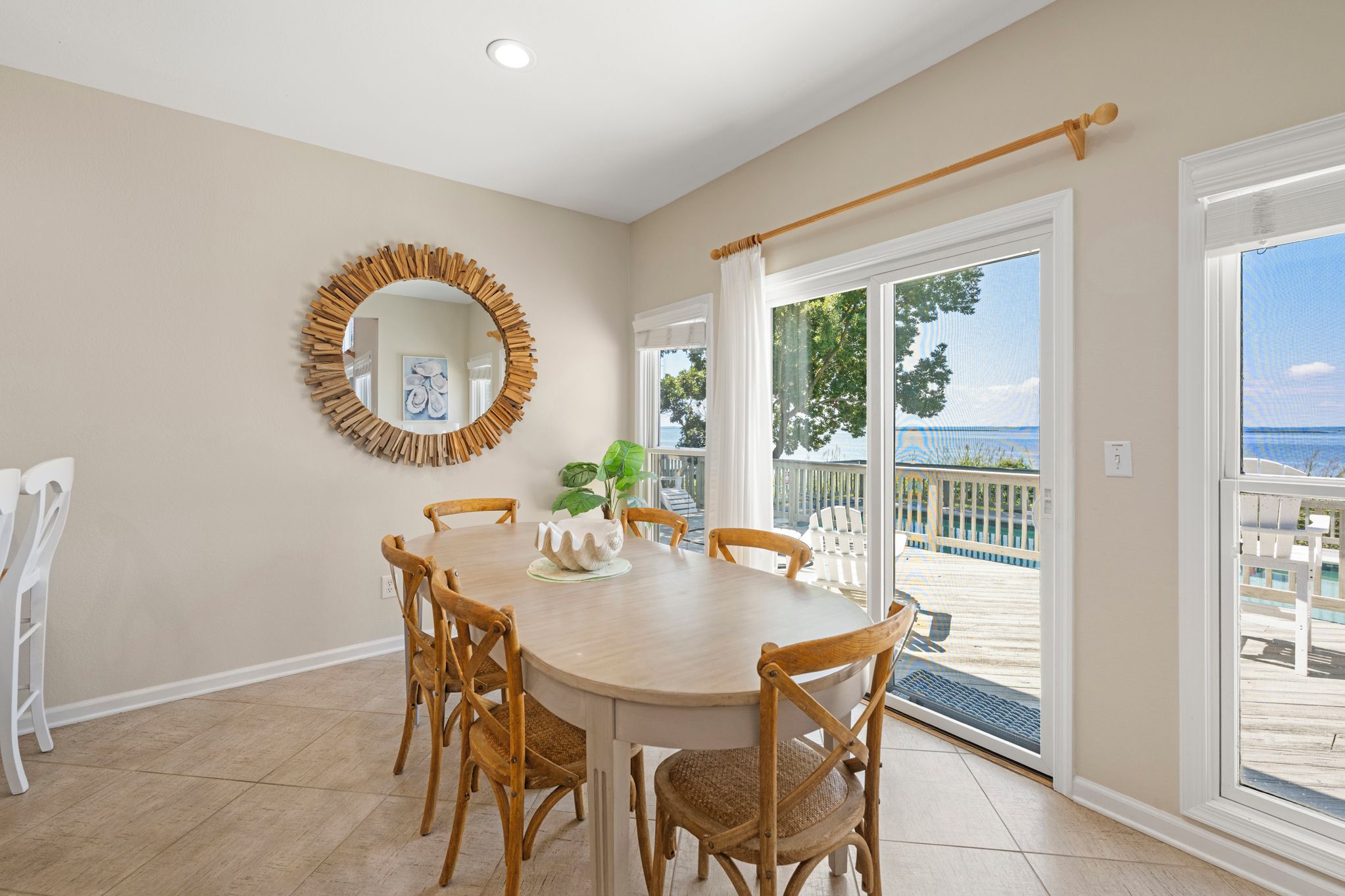 A dining area with a round table, wooden chairs, a mirror, and a view of the outdoors.