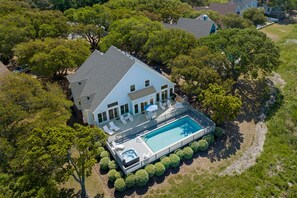 An aerial view of a house with a swimming pool, surrounded by trees and a deck with lounge chairs.