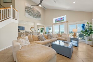 A spacious living room with a large sectional sofa, a glass coffee table, and a view of the ocean through large windows.